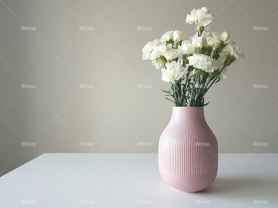 White gloves in a pink vase on a white table.