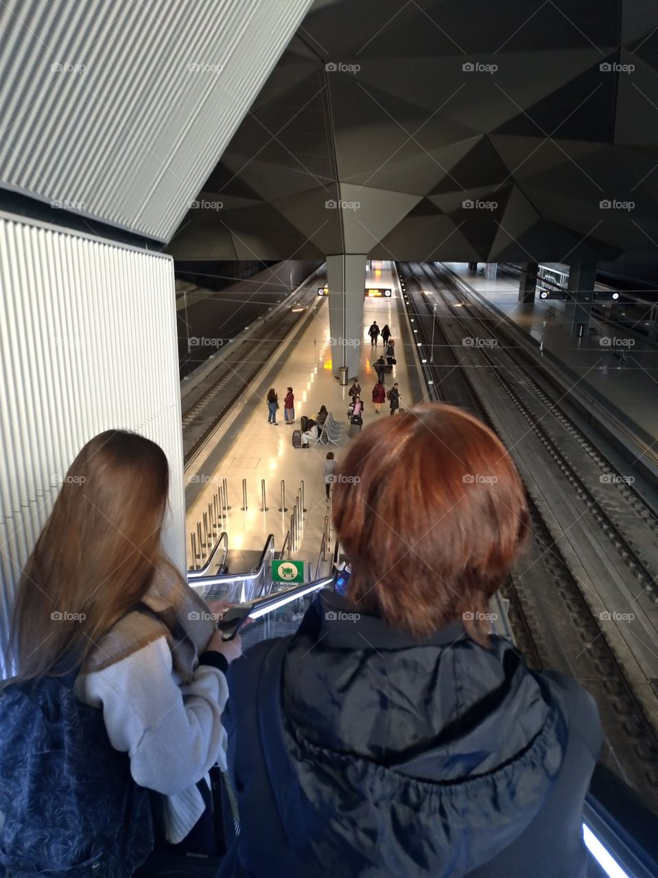 Dos chicas bajan a la estación  de tren por escalera mecánica