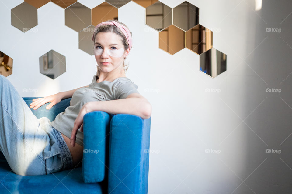 Young woman with eye patches sitting on sofa