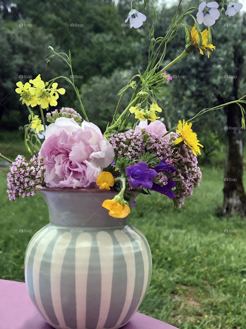 Spring flowers in a green & white striped vase on a outdoor table in a garden