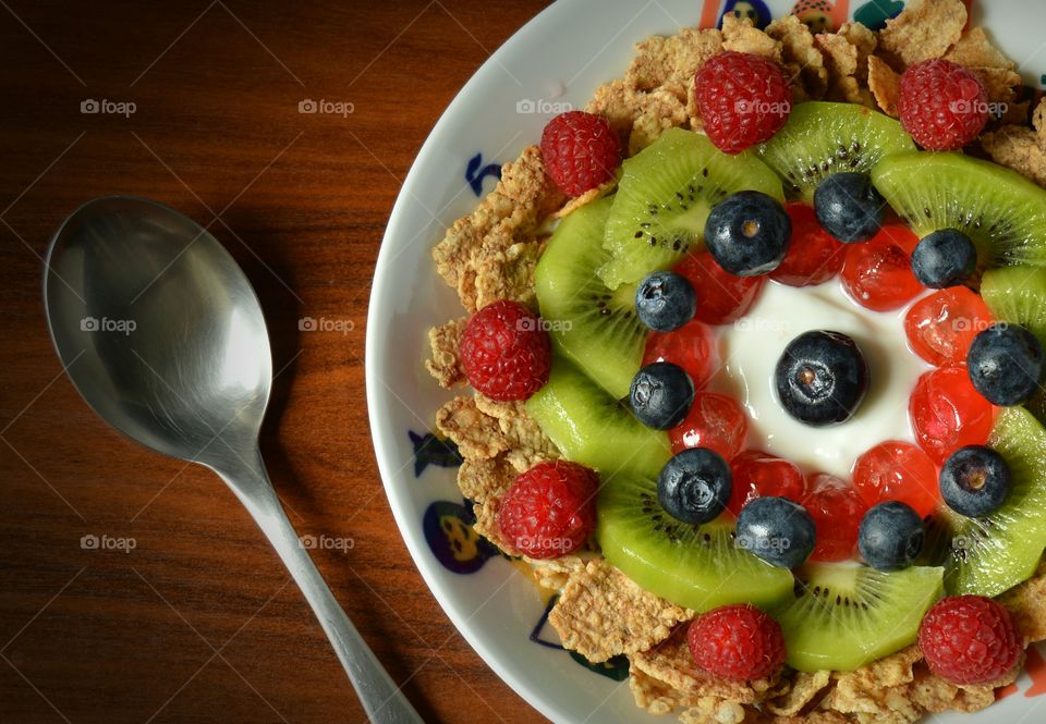 Beautifully decorated breakfast consisting of cereal, yoghurt, raspberries, kiwi, cherries and blueberries.