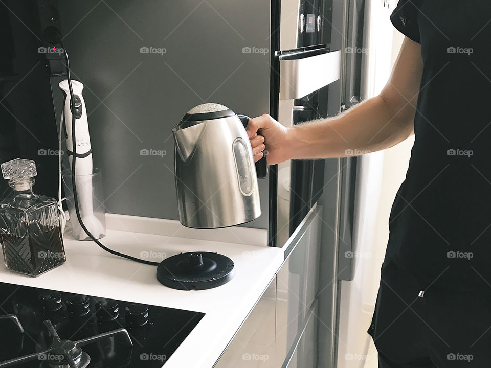Young man boiling water to prepare favorite morning coffee in the kitchen at home 
