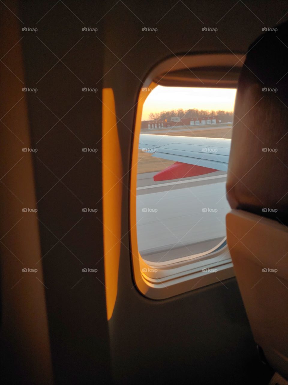A dramatic view of the interior wall of a plane highlighted with golden sunshine, offering a glimpse of runway outside.