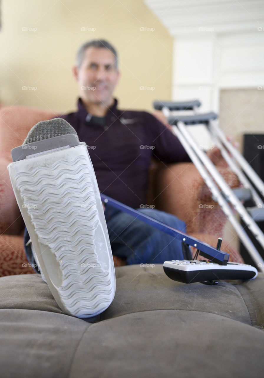 Man with broken ankle using a reacher to get the remote 