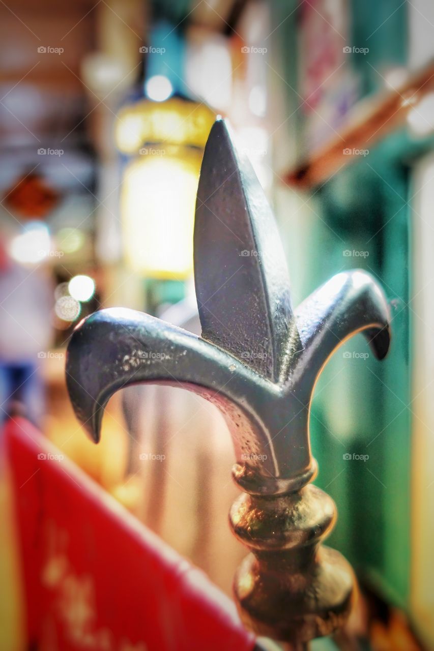 Cast iron fence ornament in the form of a Fleur de lis. Night or low light image accompanied by an out-of-focus (bokeh) background.