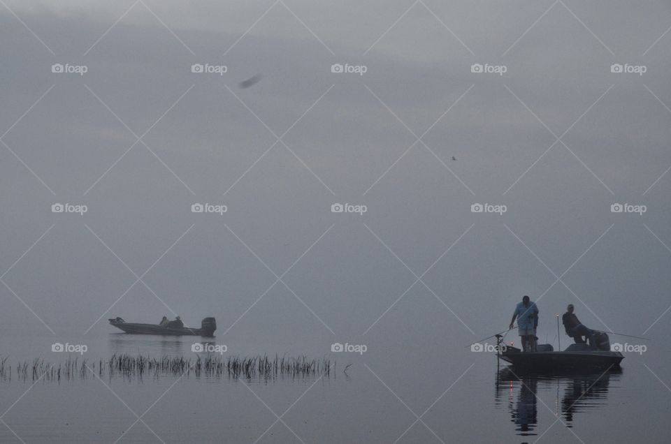 It's early in the morning, a grey foggy humid one. The boat is floating serenely on the lake. It seems that there's no distinction between the sky and the water. The people are hopeful, they might catch something. 