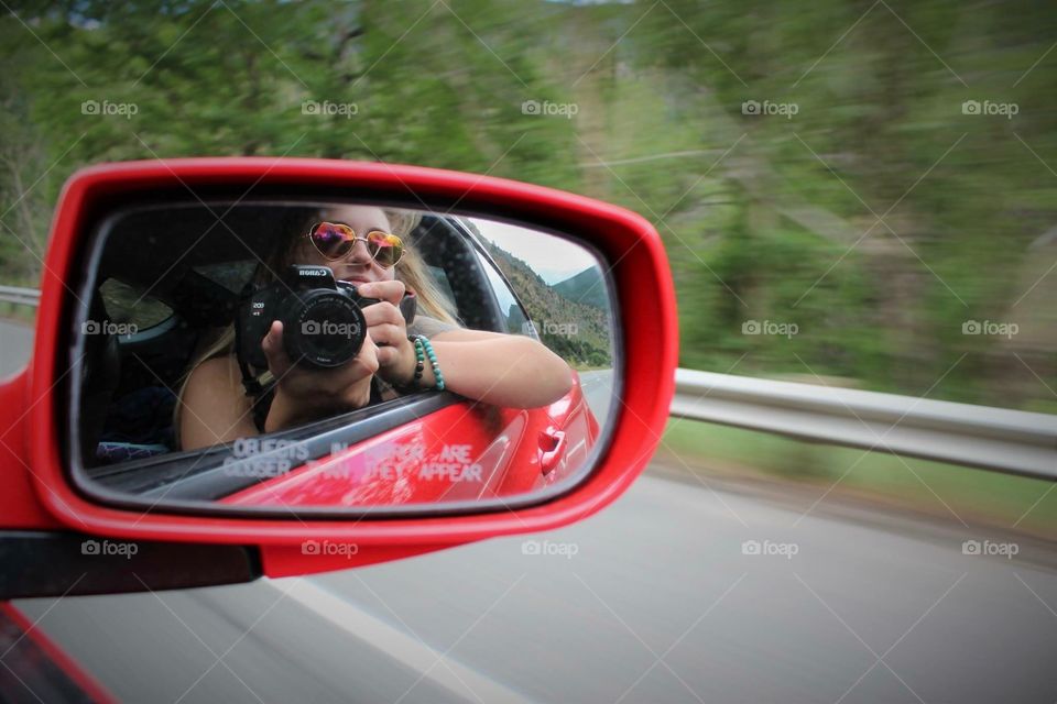 Reflection of a woman with camera in side view mirror