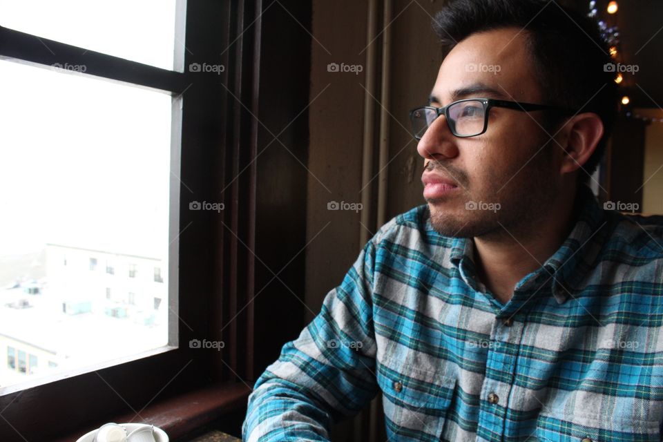 Profile closeup portrait of a young Hispanic man pensively stares out the window in a dark room