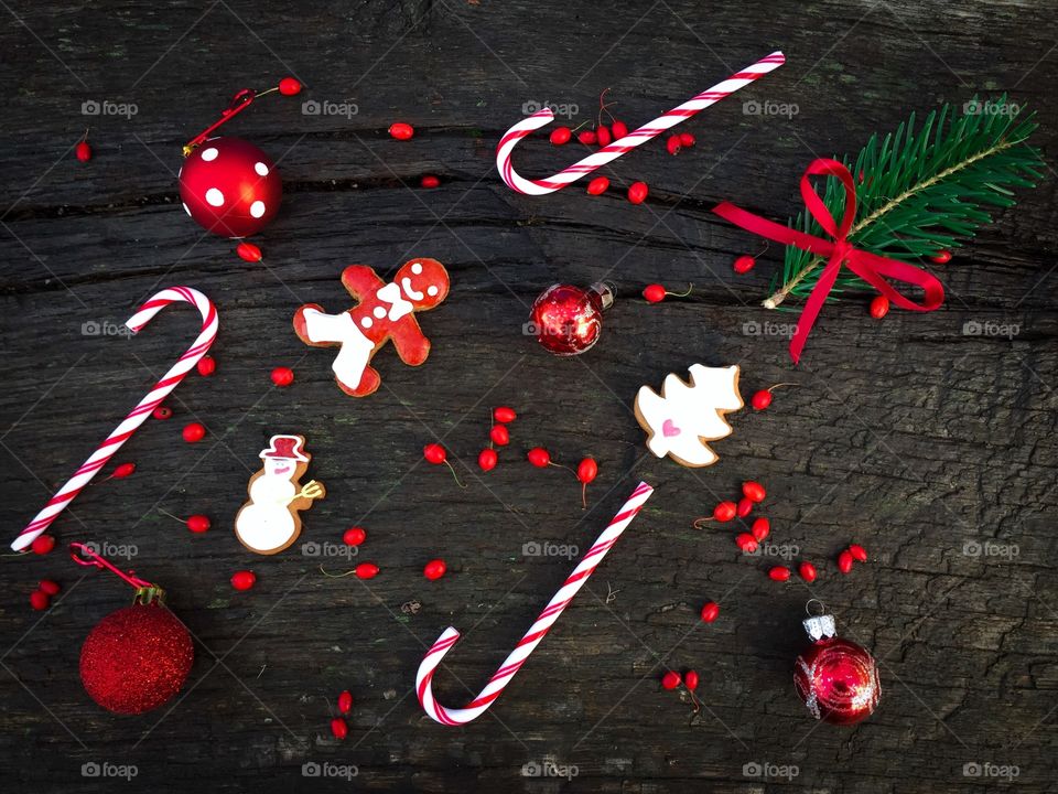 Flat lay of red and white Christmas decorations consisting of candy canes,gingerbread,red ribbon, red globes and red berries on rustic wooden table