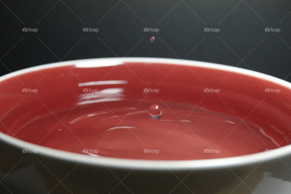 Small water drops before hitting water in red and white bowl.