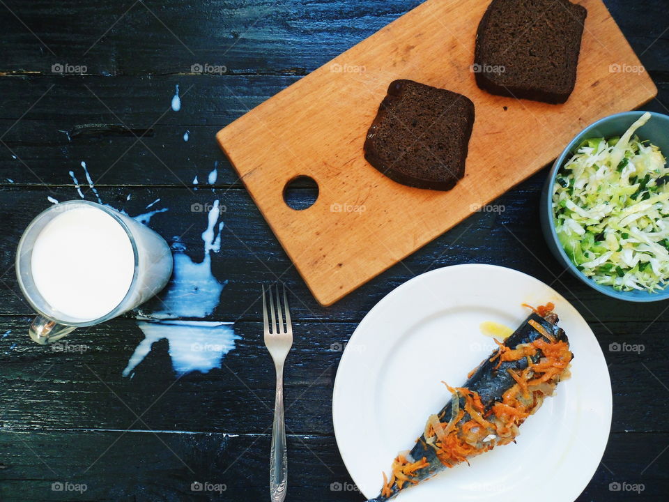 baked mackerel, vegetable salad, a cup of milk and bread on a black background, breakfast