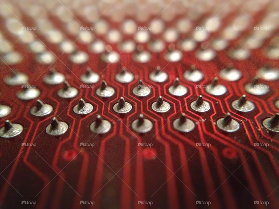 Macro close up of a Row of soldered pins on the back of a red computer motherboard. You can see the detail of the line traces weaving between the pins and fading into the background.