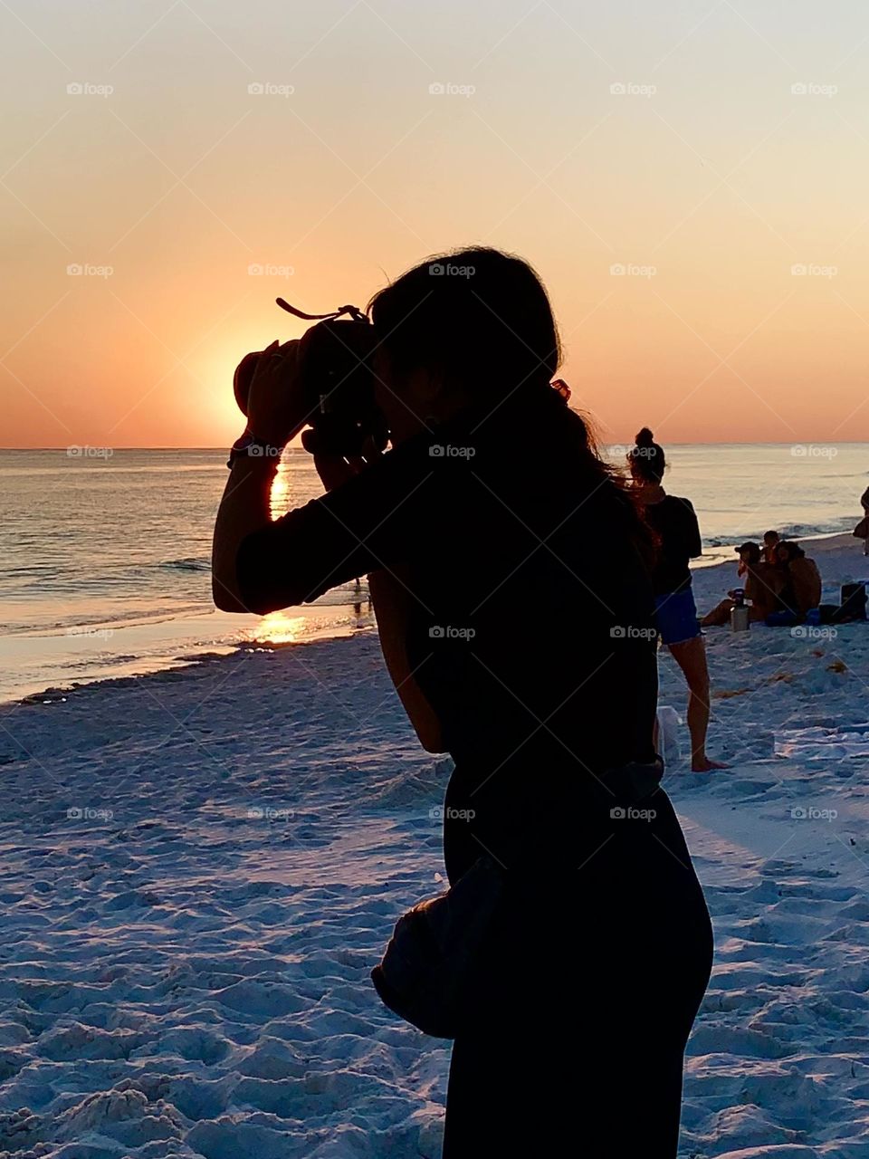 Sunset on the white sand covered beach. A young lady focuses on the descending sunset as it retreats into its slumbering place. 