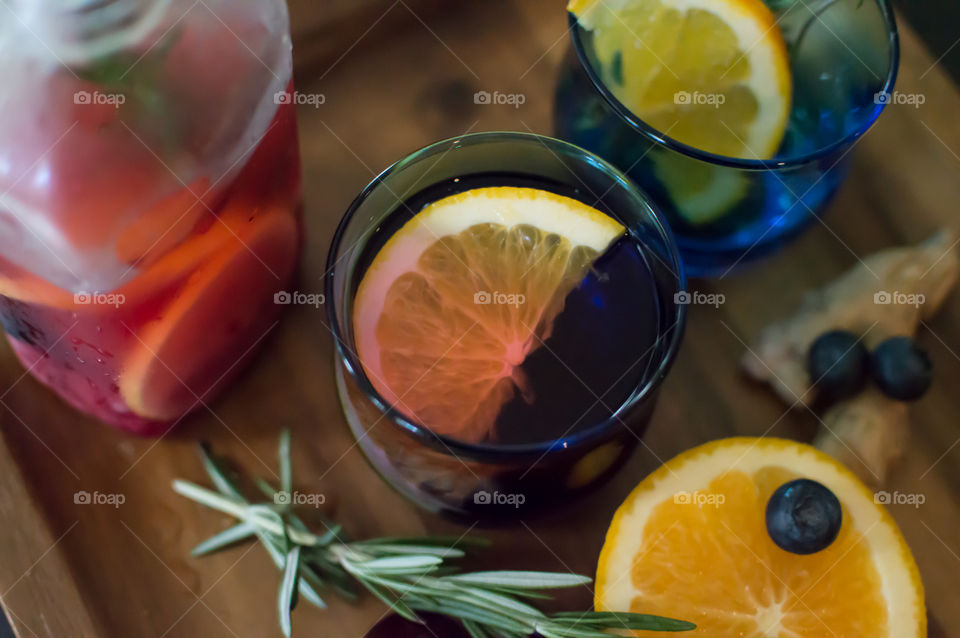 High angle view of glasses with orange slice, ginger and rosemary with blueberry ingredients next to beautiful home made aromatic flavored water ready to serve healthy summer drinks