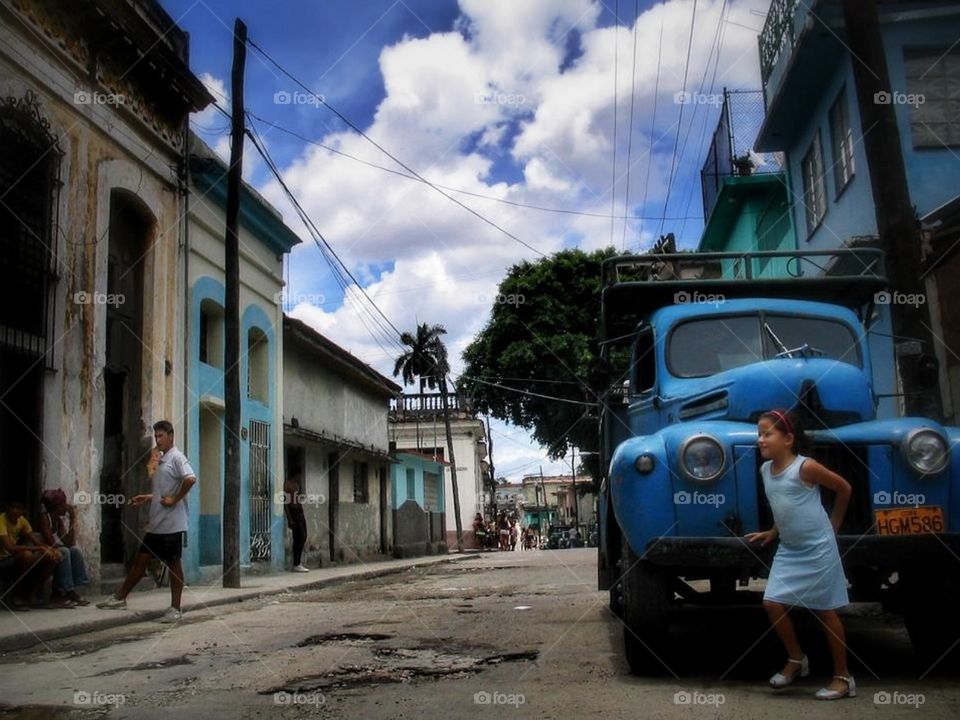 Little girl hiding in the front of a blue car.