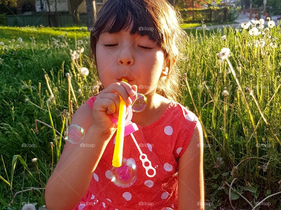 Cute girl in a red polka dot dress is blowing soapy bubbles