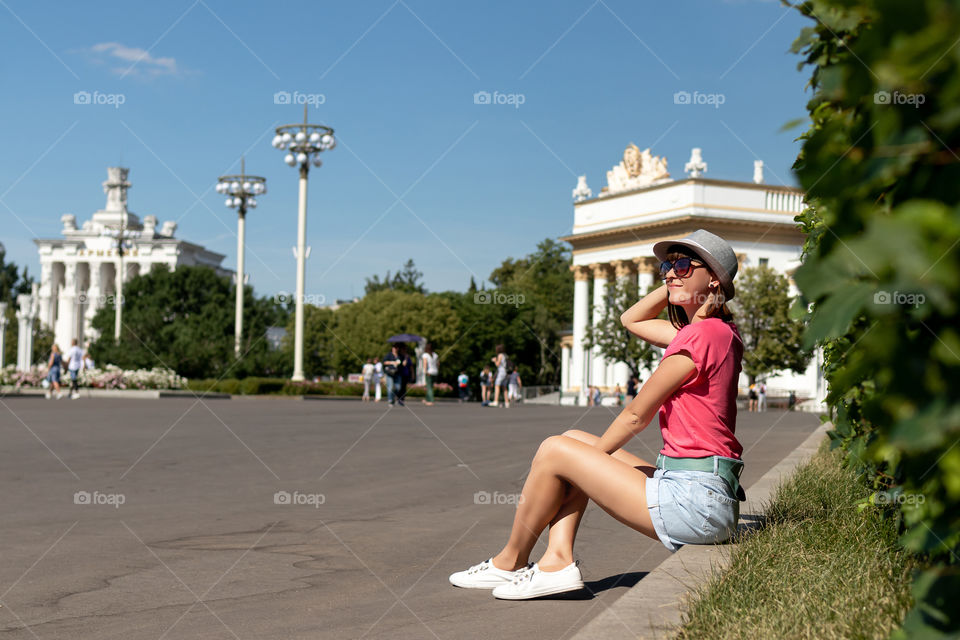 The girl in the hat sits on the curb in the park VDNH. Moscow city.