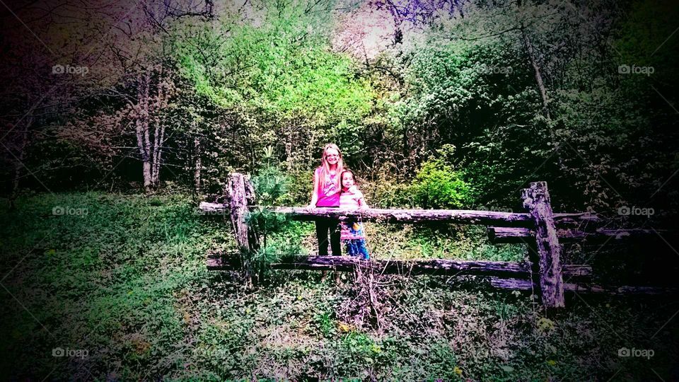 Two sisters standing behind an old wooden fence on a mountain.