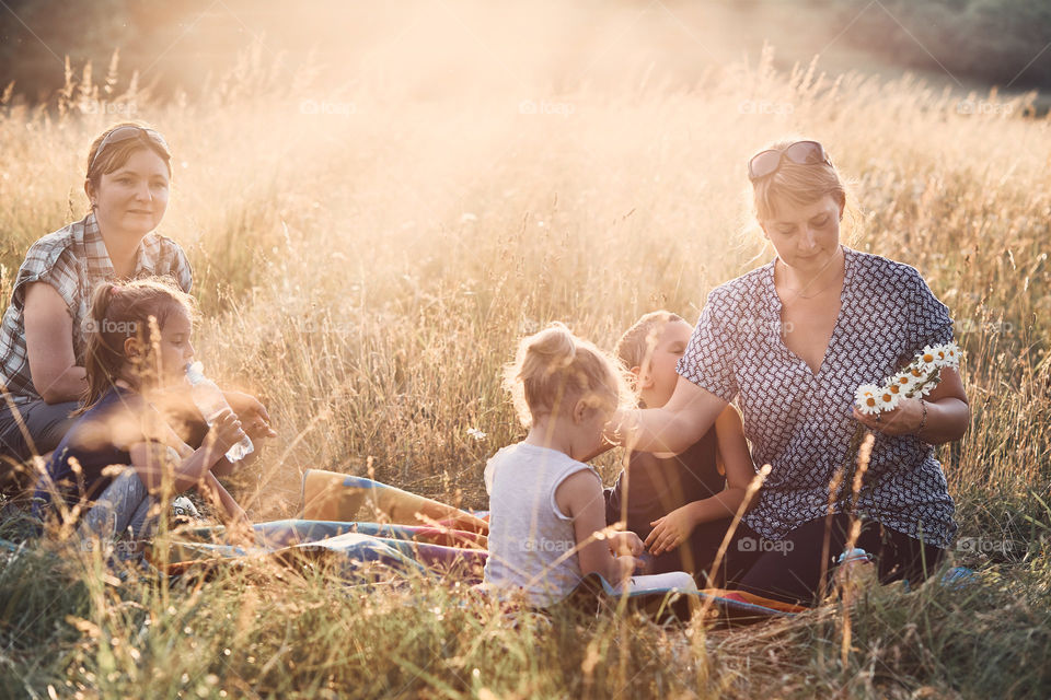 Family spending time together on a meadow, close to nature, parents and children playing together, making coronet of wild flowers. Candid people, real moments, authentic situations