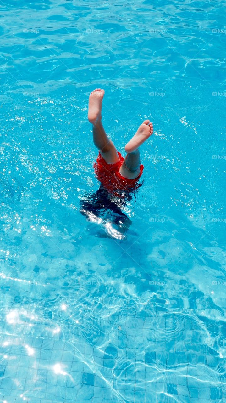 Young kid dives into pool. Young kid having fun on vacation at swimming pool takes a messy plunge diving into water