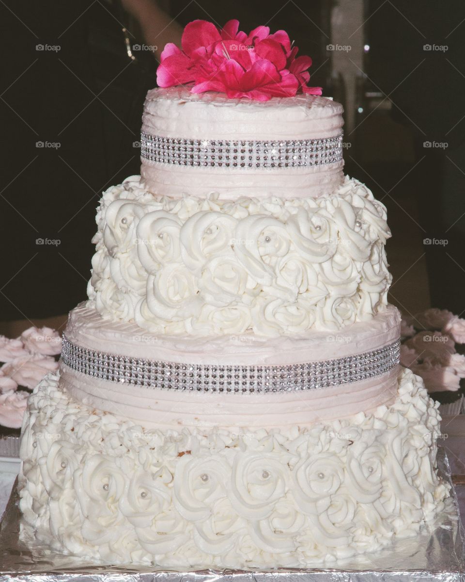 A fancy cake with massive pink flowers and decorated with glitter and white flowers