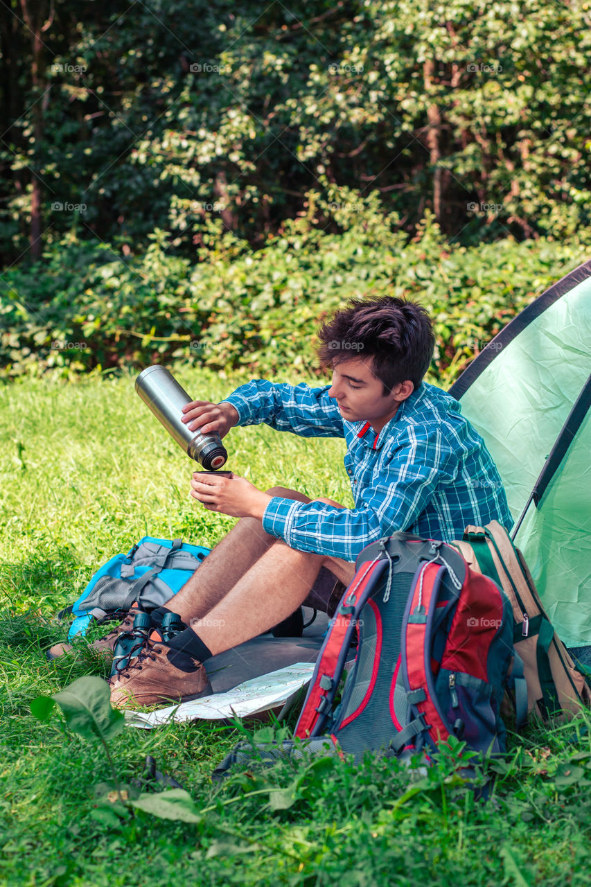 Spending a vacation on camping. Preparing a meal outdoor. Young man planning next trip and drinking a coffee