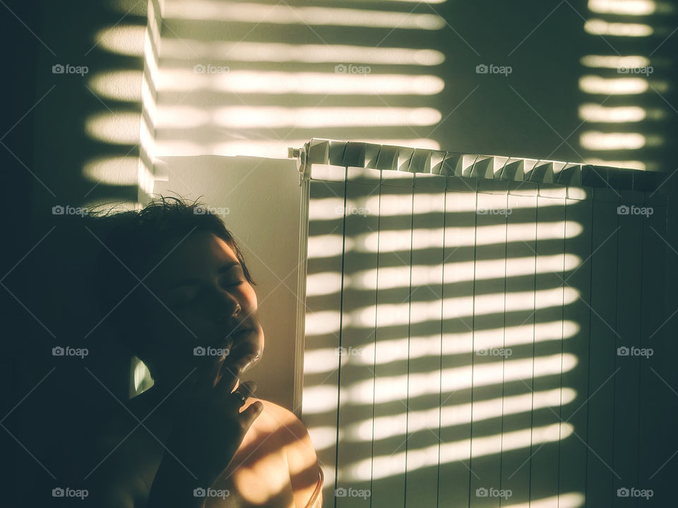 Play of light and shadow.  Portrait of a young woman at home against a background of a white wall with shadows.