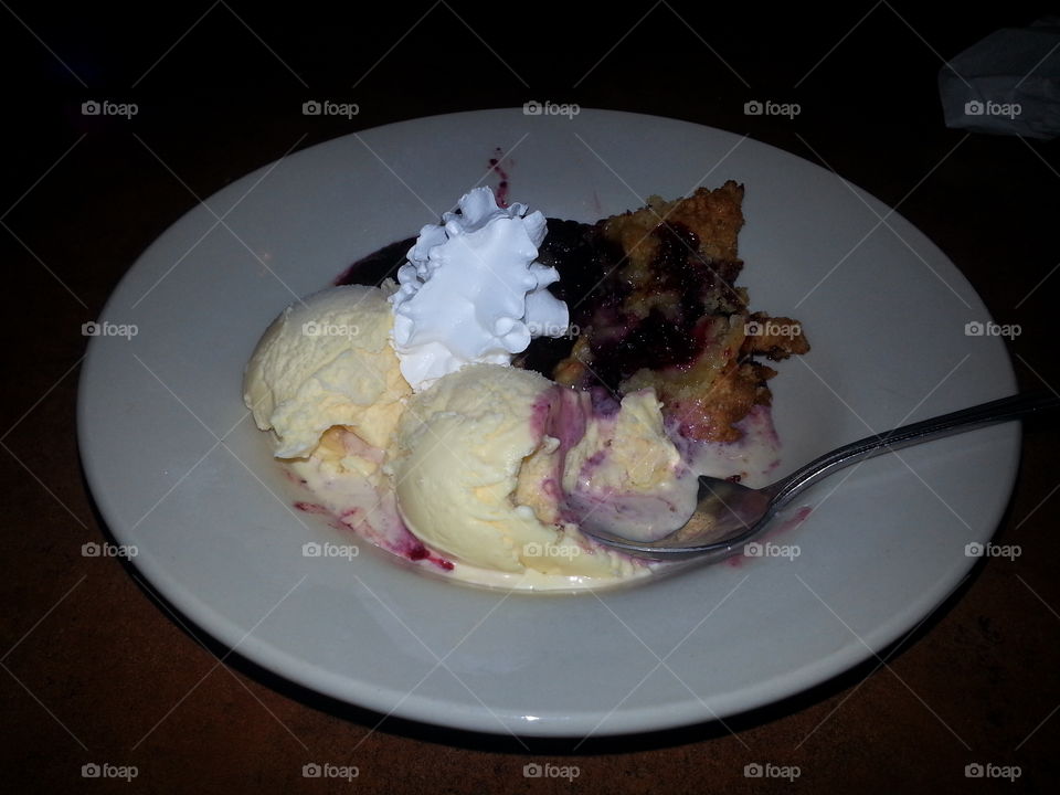 blueberry cobbler & ice cream. freshly baked blueberry cobbler with vanilla ice cream and whipe cream served for dessert at a restaurant.