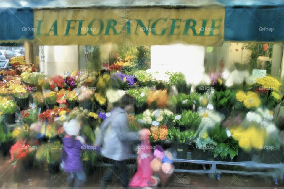 A view out of a bus window onto a Paris street florist on a very wet day, water pours down the windows, creating a blur of colours