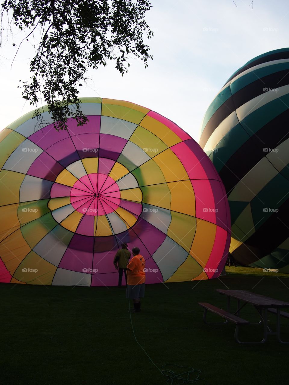 Two bright and colorful hot air balloons on the grass of Ochoco Park filling with helium for a morning flight over Prineville in Central Oregon on a beautiful summer morning as the sun rises.
