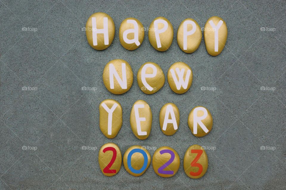 Happy New Year 2023 composed with yellow colored stones over green sand