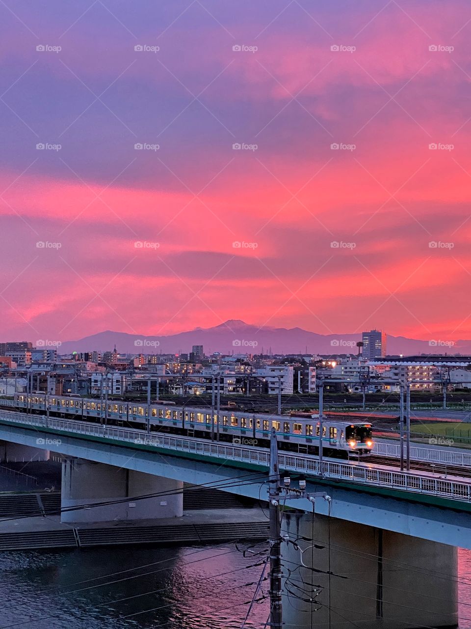 Psychedelic pink sunset over mountain (Mt Fuji) and train in the foreground with its lights on