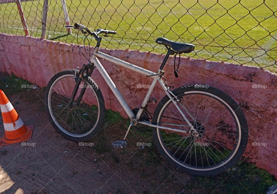 going to soccer practice by bike. A white bycicle left by a football field