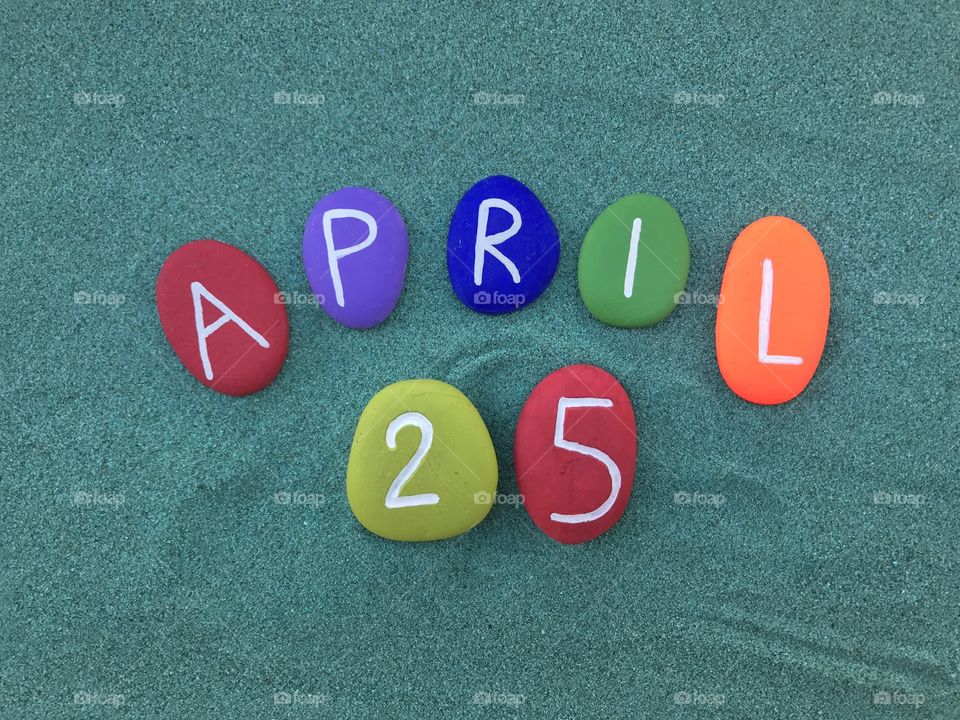 25 April, calendar date with colored stones over green sand 