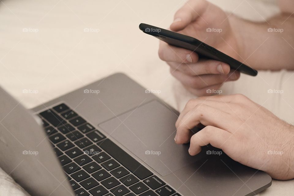 A man holding a phone and using his laptop computer