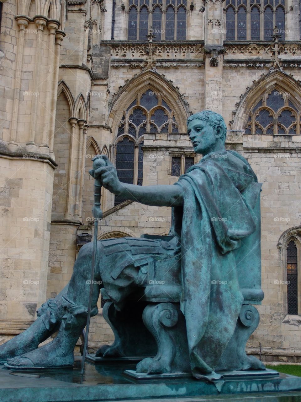 An old copper statue turned a beautiful green of a Roman figure in front of a gothic church in England. 