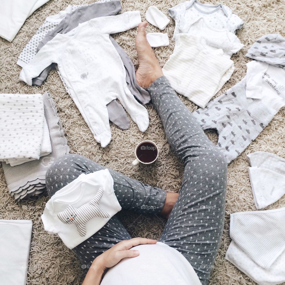 Preparing to be a mom, baby clothes on the carpet, top view, pregnant