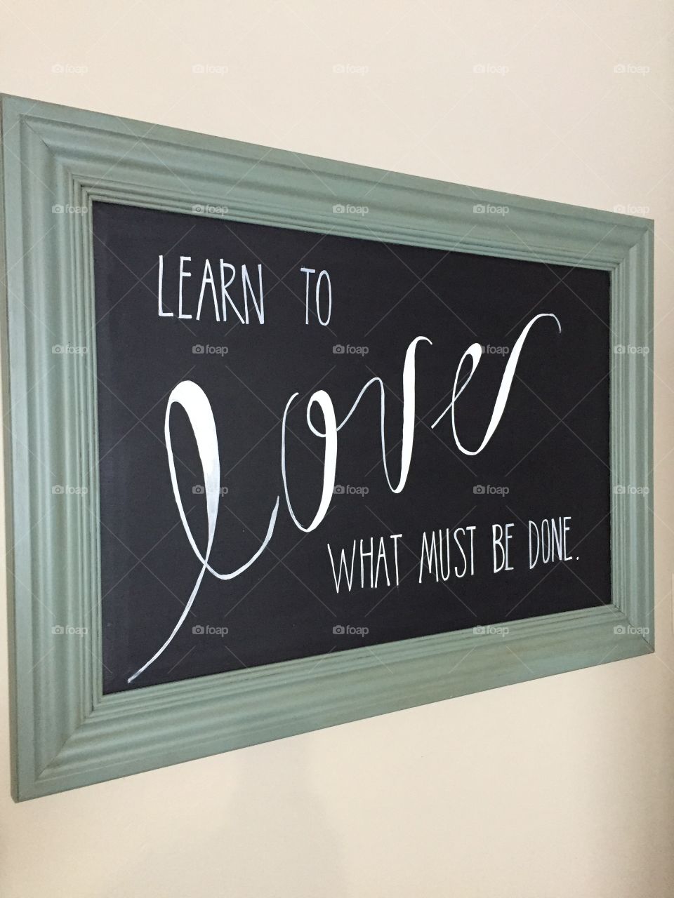 Learn To Love What Must Be Done. Written with white paint on a black board.