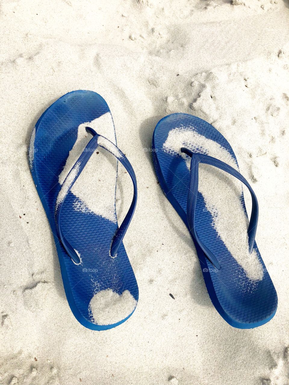 Blue flip-flops sitting in the sand.