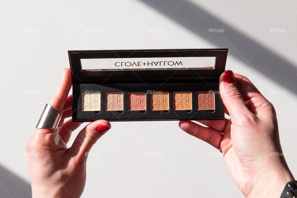 Hard light product shot of a woman holding an eyeshadow palette 