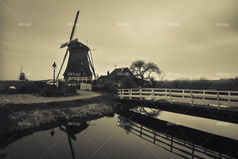 Scenic view of a windmill and bridge near a canal in The Netherlands. Monochrome photograph.