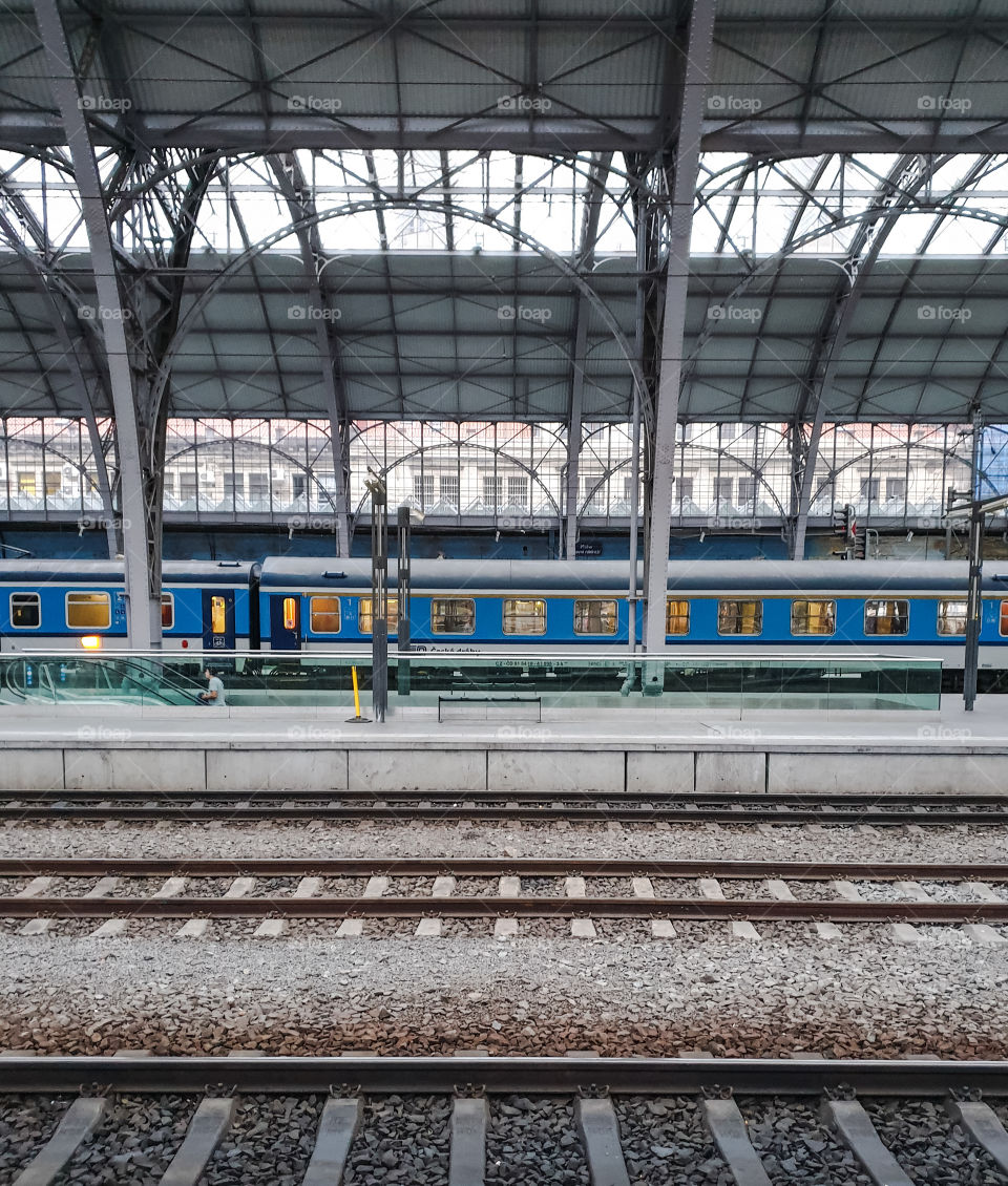 Prague, the main railway station. A blue passenger train in the windows of which the light is on awaits boarding passengers on a platform with a glass roof