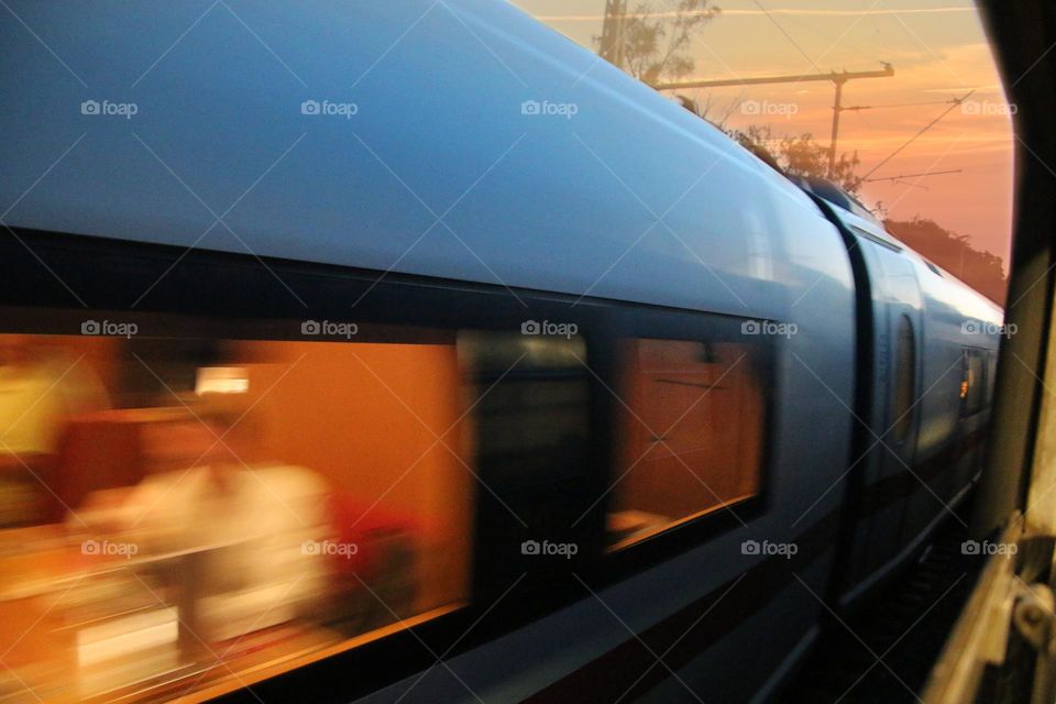 Closeup from a train window on a passing train with illuminated windows and one person at sunset