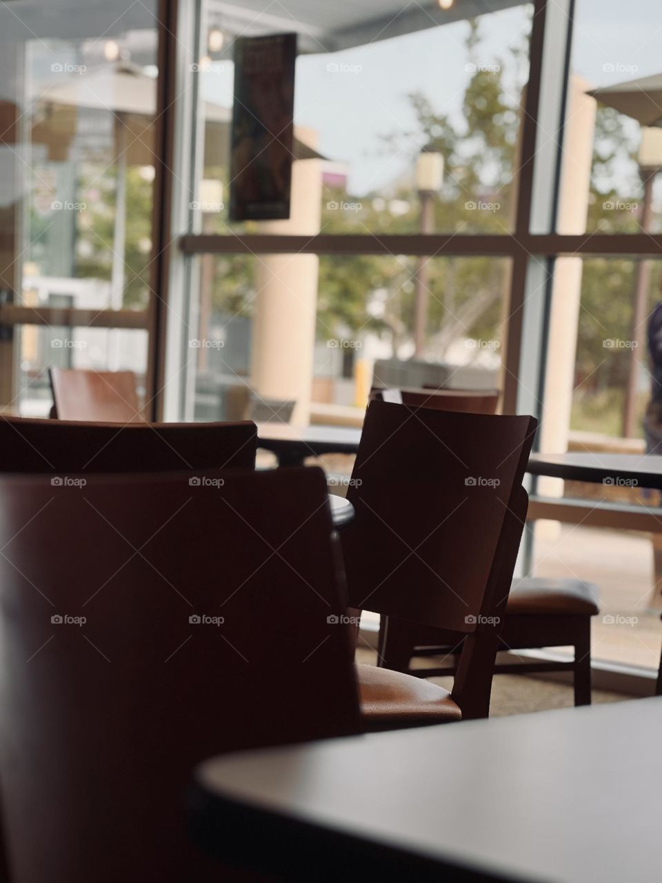 Cafe interior - clean lines closeup of hardbacked wooden chair and table edge with bokeh effect natural window light in background 