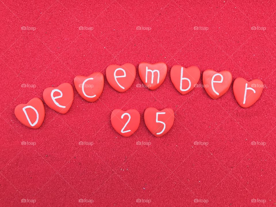 25 December, Christmas date with red painted heart stones letters over red sand

