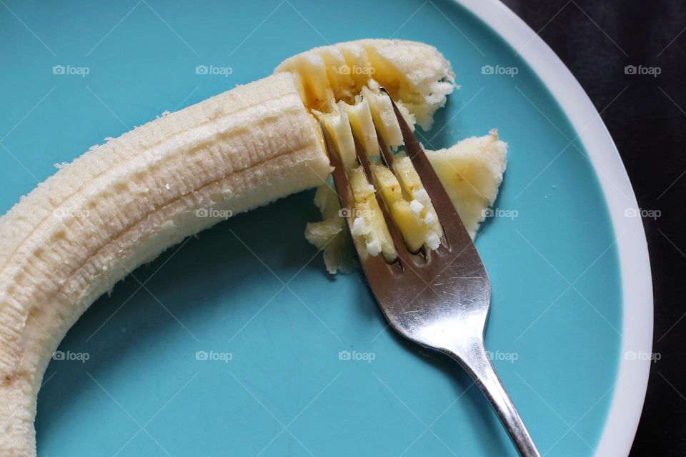 A banana is mashed by a fork on a blue plate
