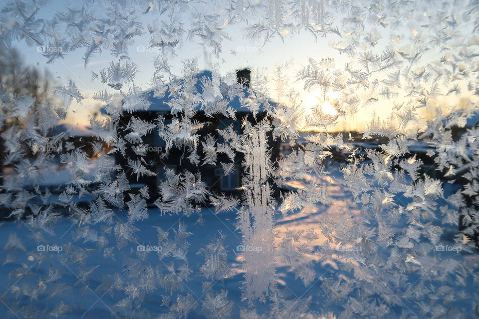 Window with a frosty pattern against the background of the low winter sun. December in the Russian hinterland