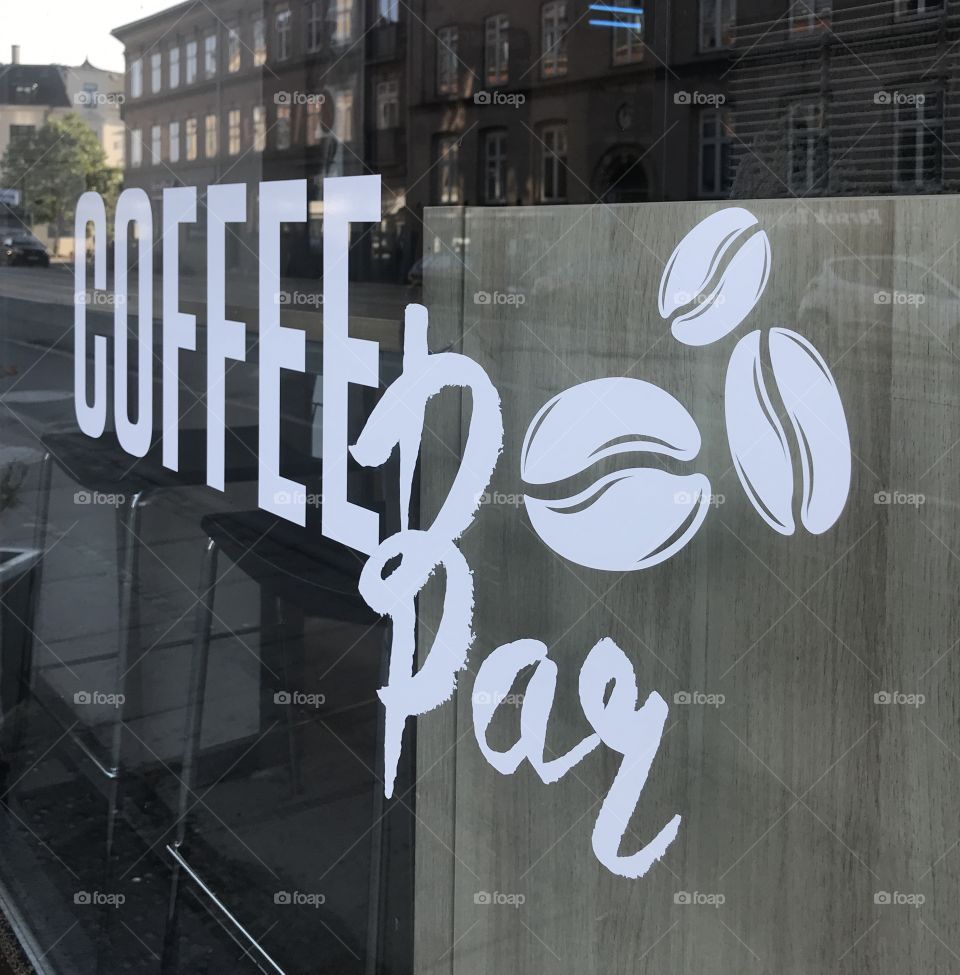 Coffee bar wrotem on shop window. Reflections in window of buildings on the other side.