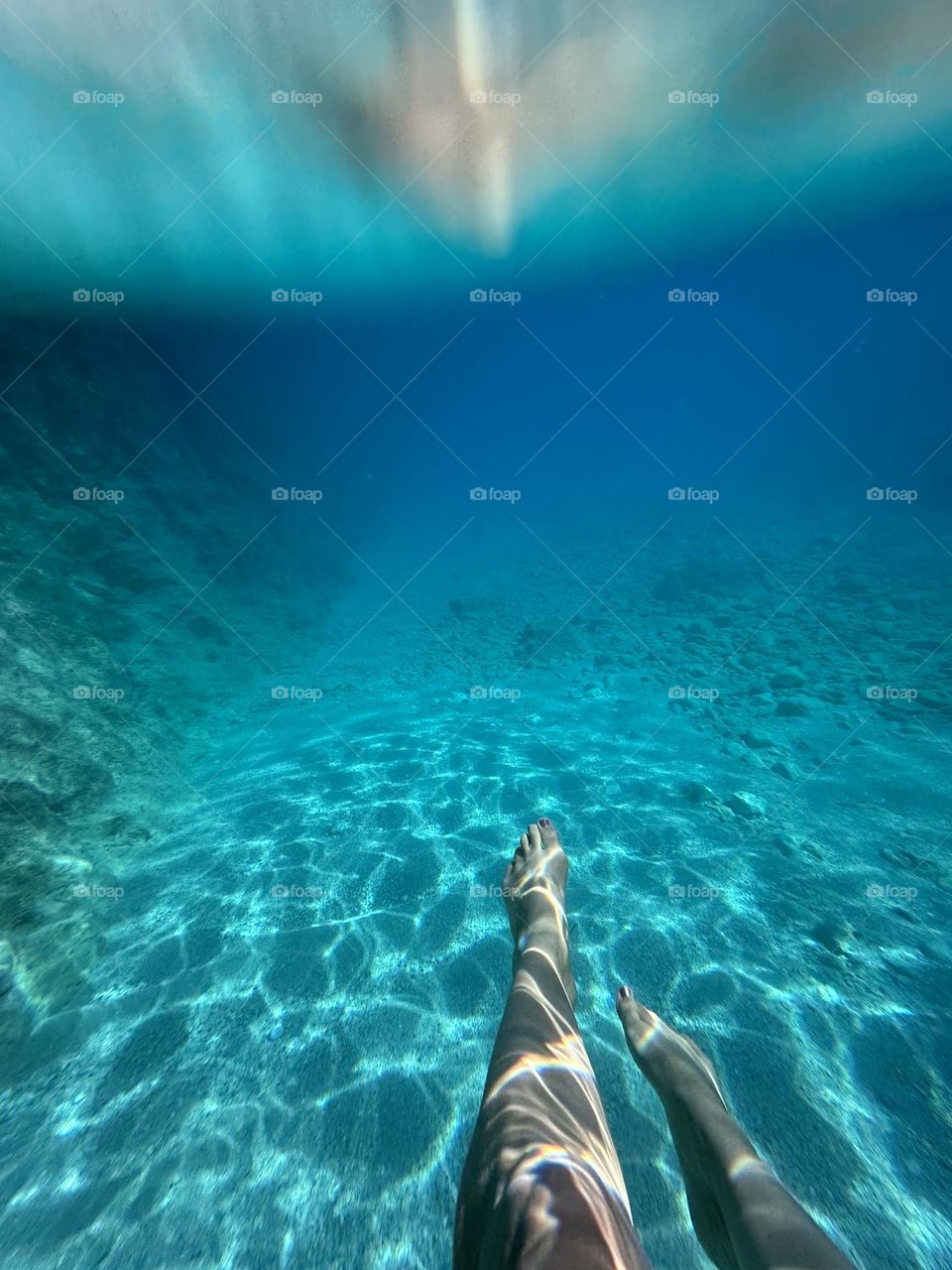 Clear blue underwater view of swimmers legs with the sun sparkling 