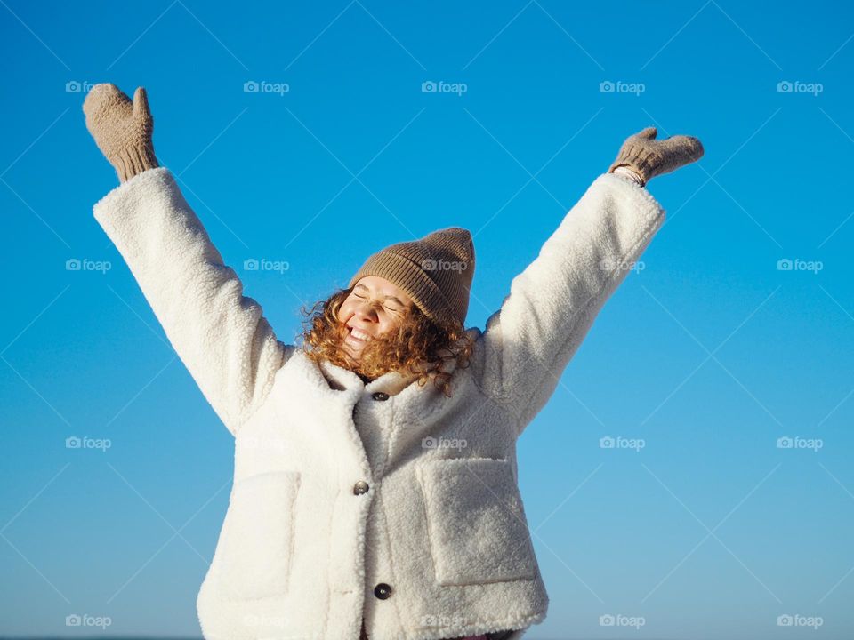 Young happy woman with curly hair in fur coat and hat having fun in winter walk
